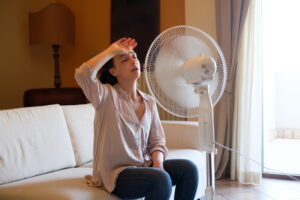 woman-sitting-on-couch-in-front-of-fan-with-hand-to-forehead